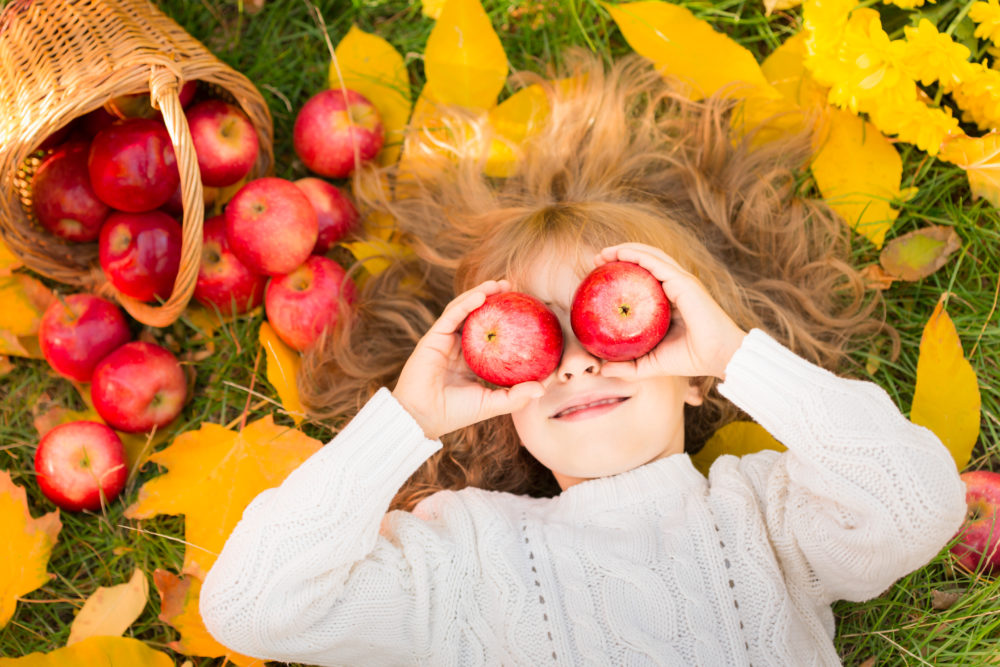 Happy child lying on fall leaves. Funny kid outdoors in autumn park